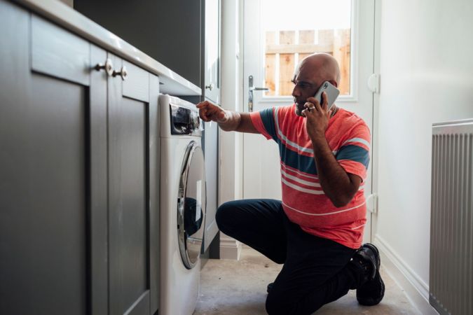 A person places a phone call while examining a washing machine.