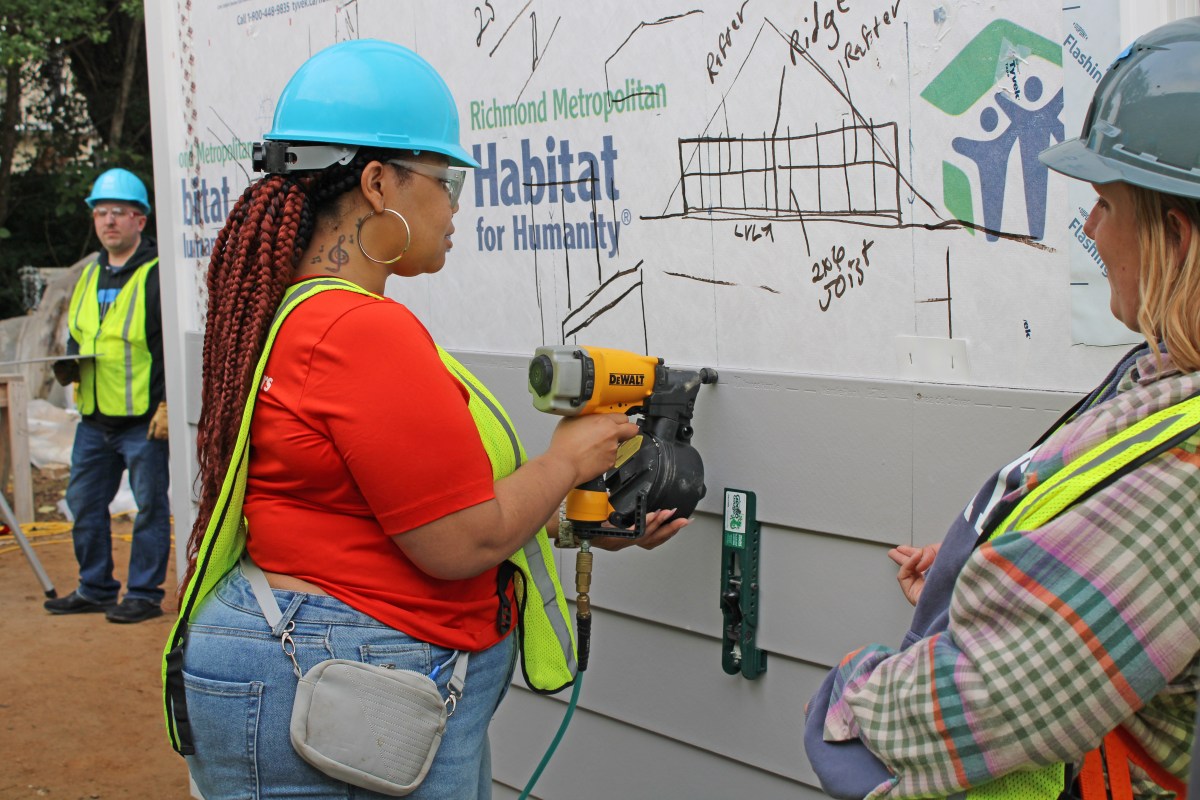 A woman wearing a hard hat uses a power tool during a Habitat for Humanity Pride Build in Richmond.