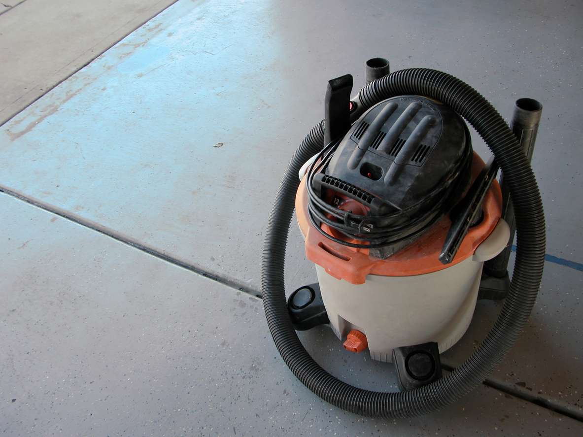 A shop vacuum sitting on the garage floor between cleaning up messes.