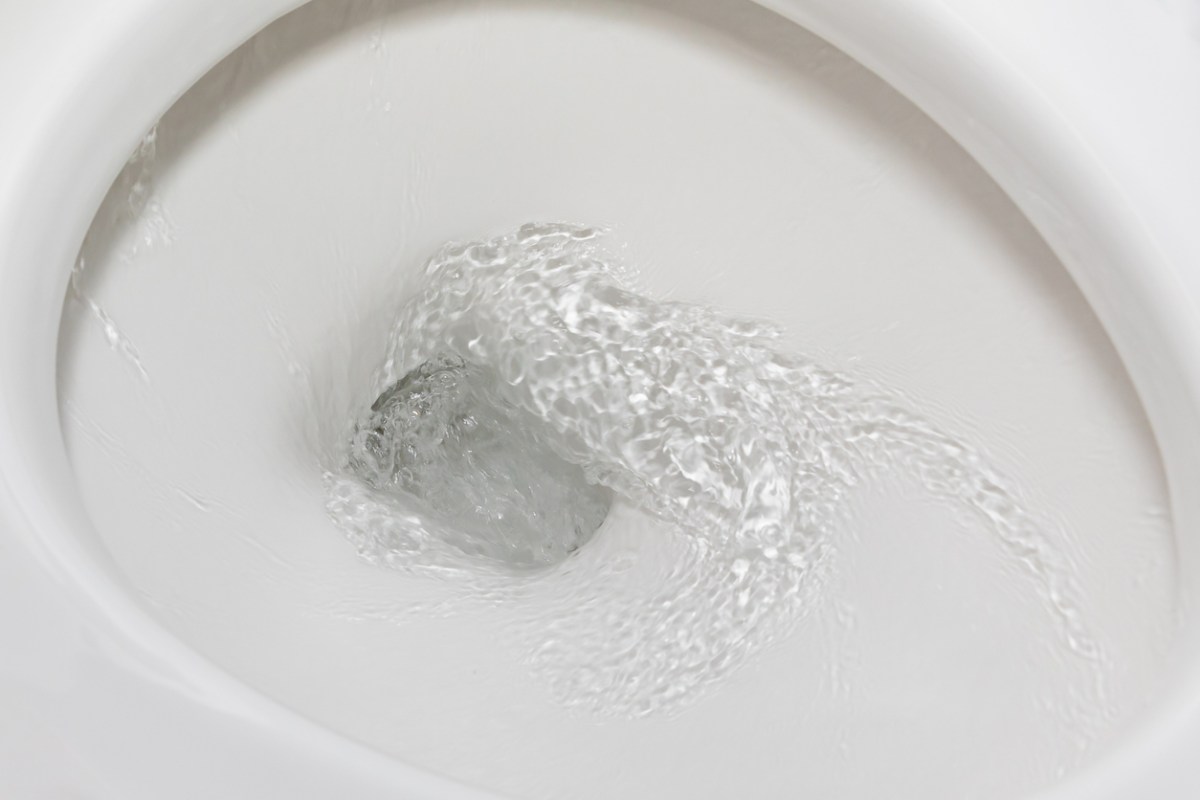 A white toilet bowl is mid-flush, with water spiraling down its clean porcelain.