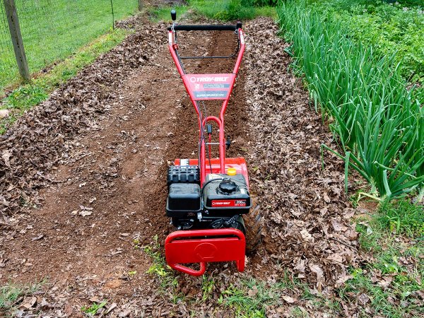 Red Troy-Bilt Super Bronco CRT rototiller in a row of tilled garden dirt