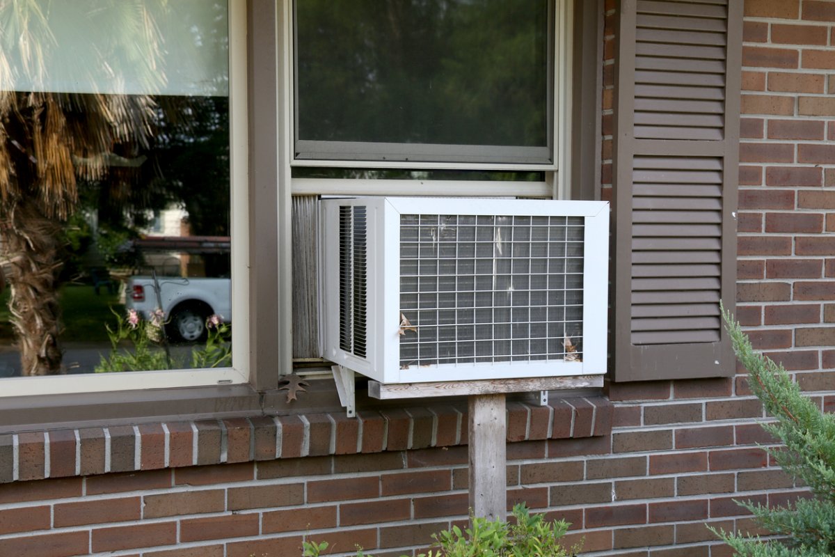 An air conditioner is seen in the window of a brick house.