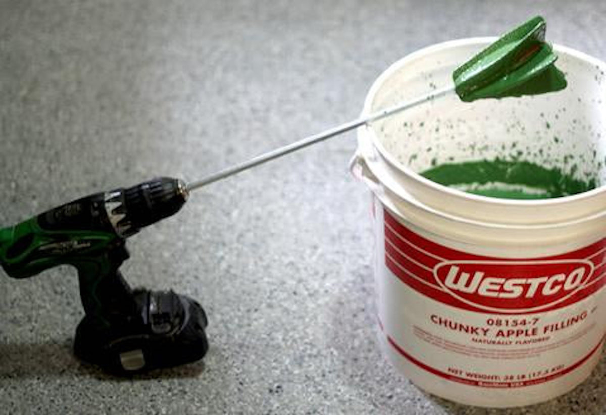 A paint mixer is attached to a drill to mix flour paste, sand, and natural pigment to create green natural clay paint.