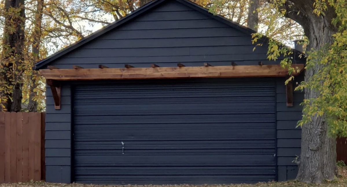 Brown wood pergola over the door of a modern charcoal grey, standalone garage.