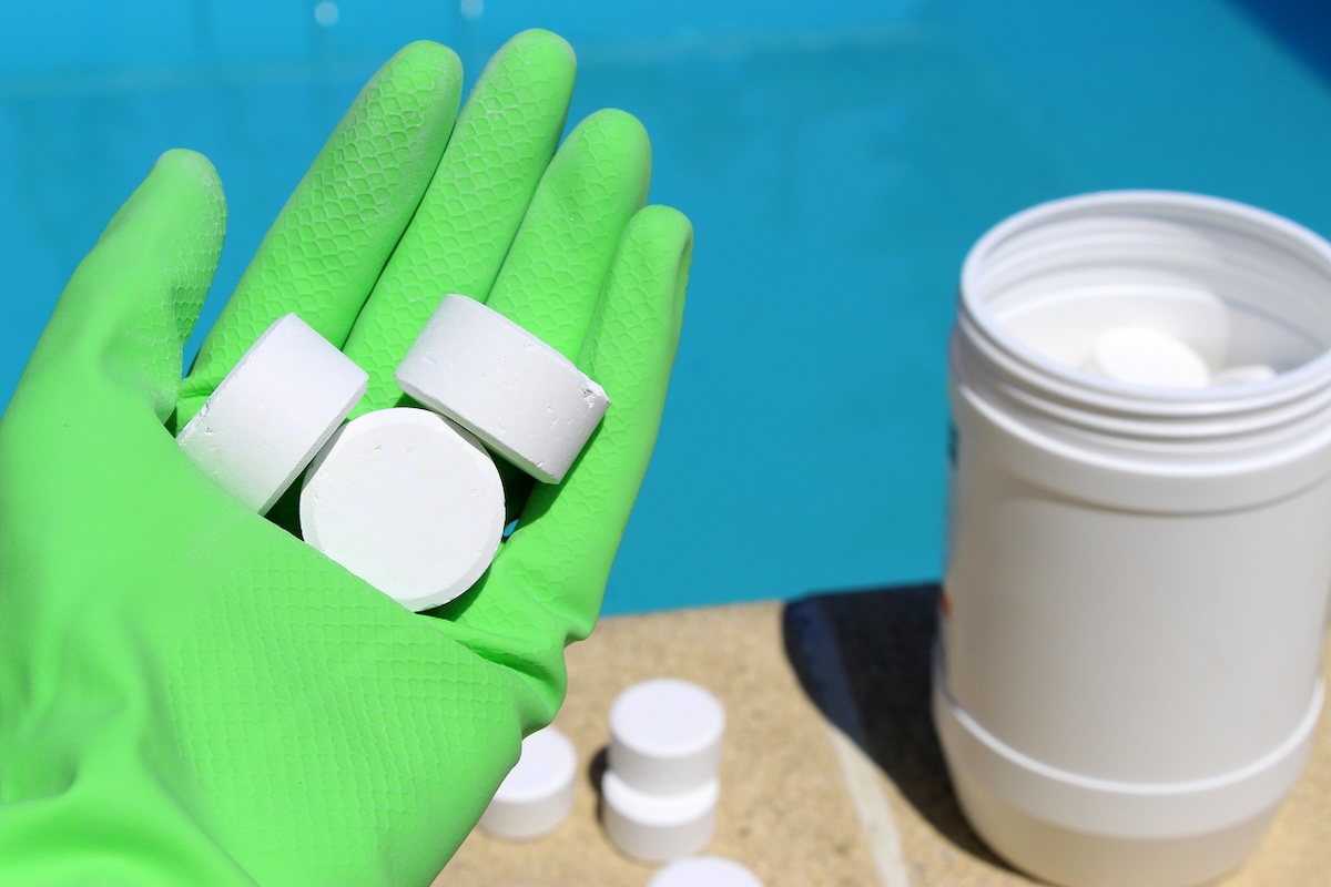 Holding tablets of white pool shock while wearing green gloves.