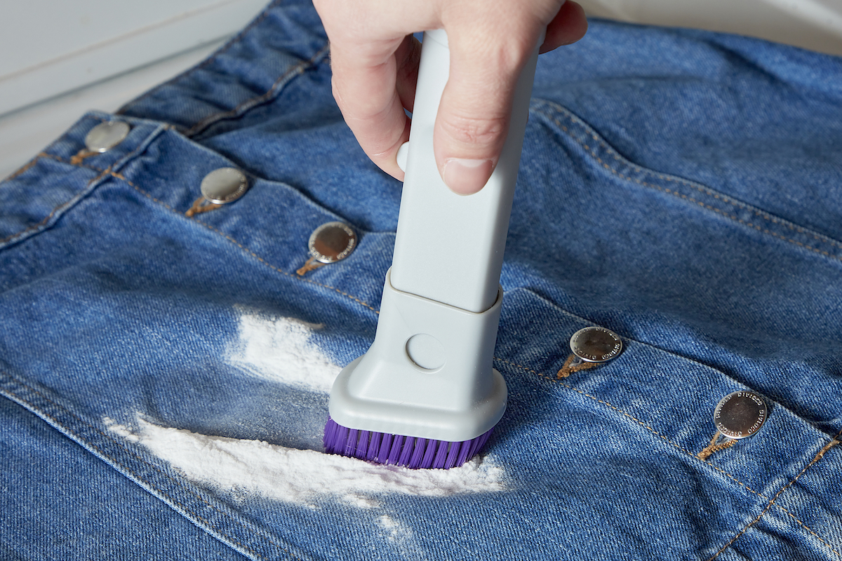 Woman uses a small scrub brush to brush baking soda off a stain on a denim skirt.