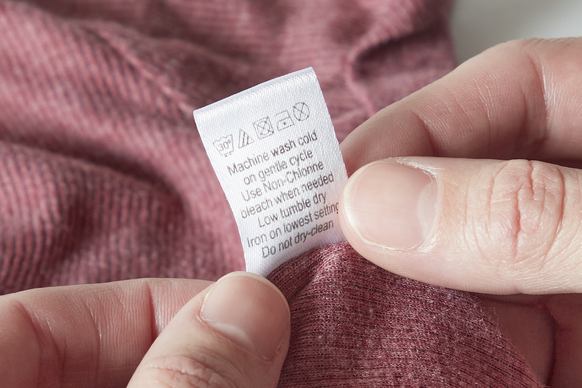 Woman consults the back of a laundry tag on a T-shirt.