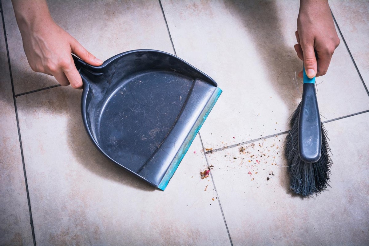 A close up of a person sweeping dirty tiles with a dustpan.