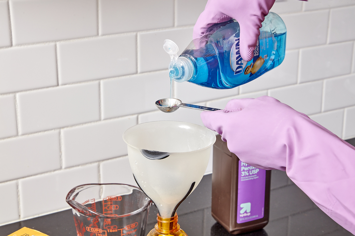 Woman adds dish soap to homemade grout cleaner recipe.