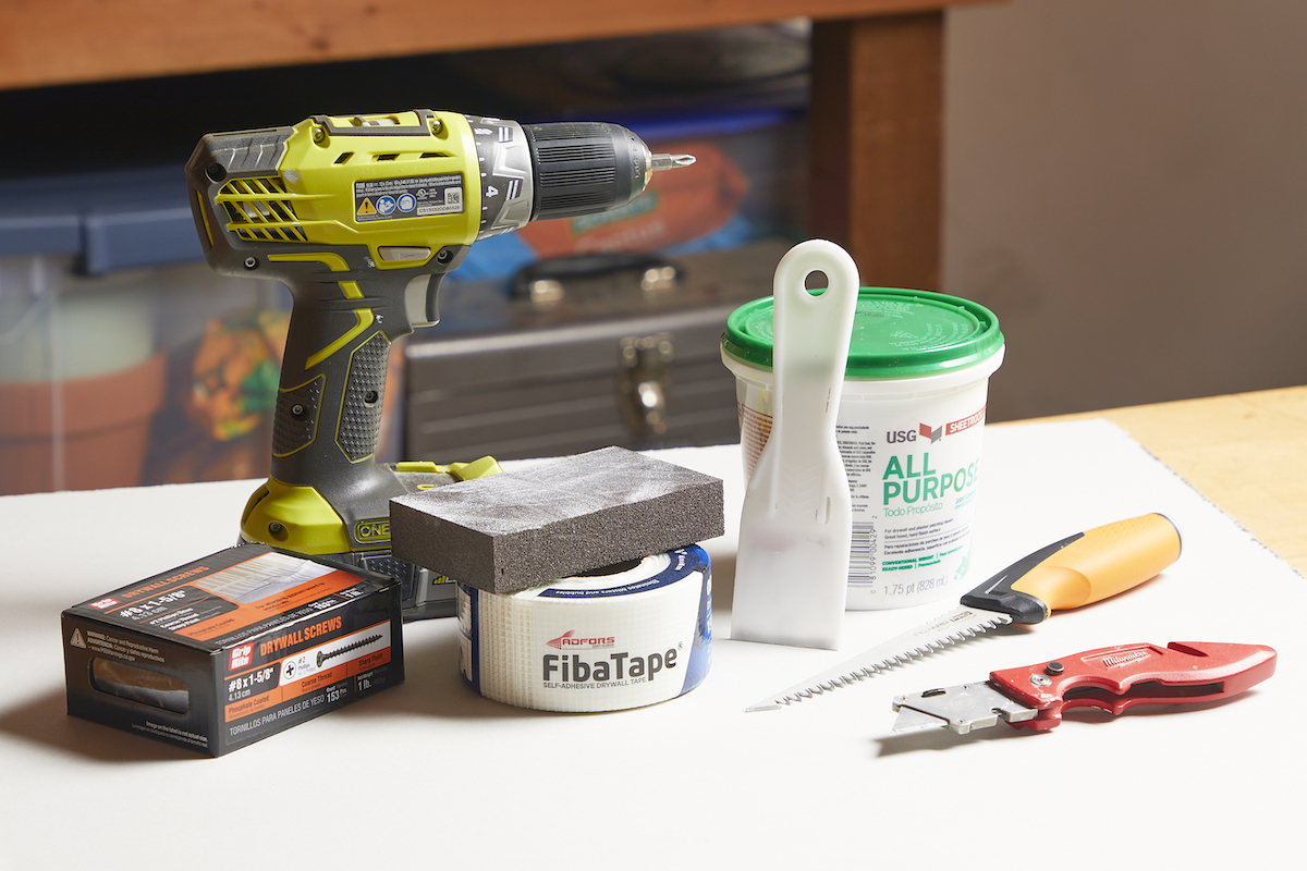 Screwdriver, joint compound, drywall saw and other drywall repair materials on a table.