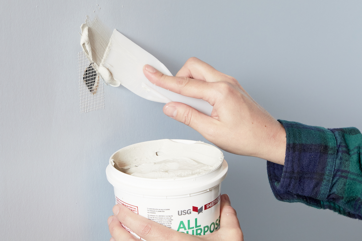 Woman uses putty knife to spread joint compound over mesh drywall tape.