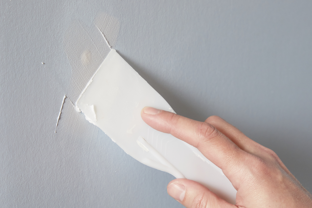 Woman swipes a putty knife over a drywall hole filled with joint compound.