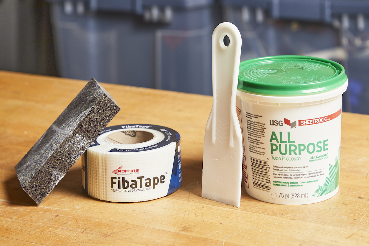 Drywall tape, sanding block, putty knife, and joint compound on a table.