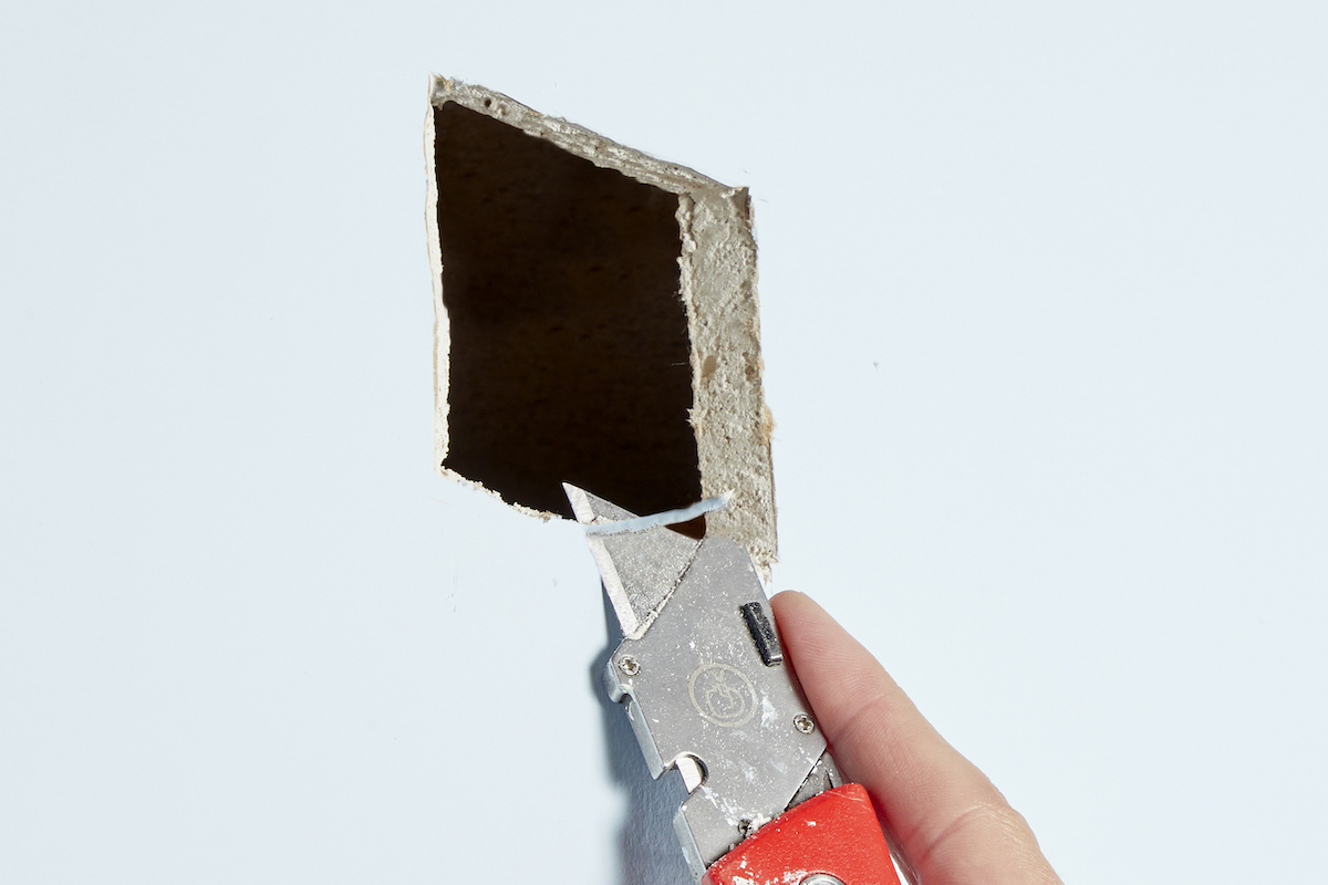 Using a utility knife to clean up a cut hole in drywall.