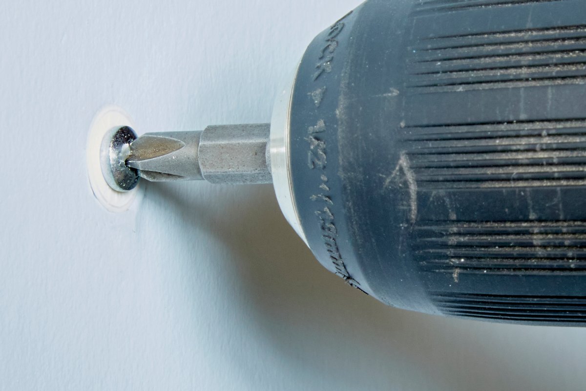 Using a screwdriver to twist a drywall anchor out of the wall.