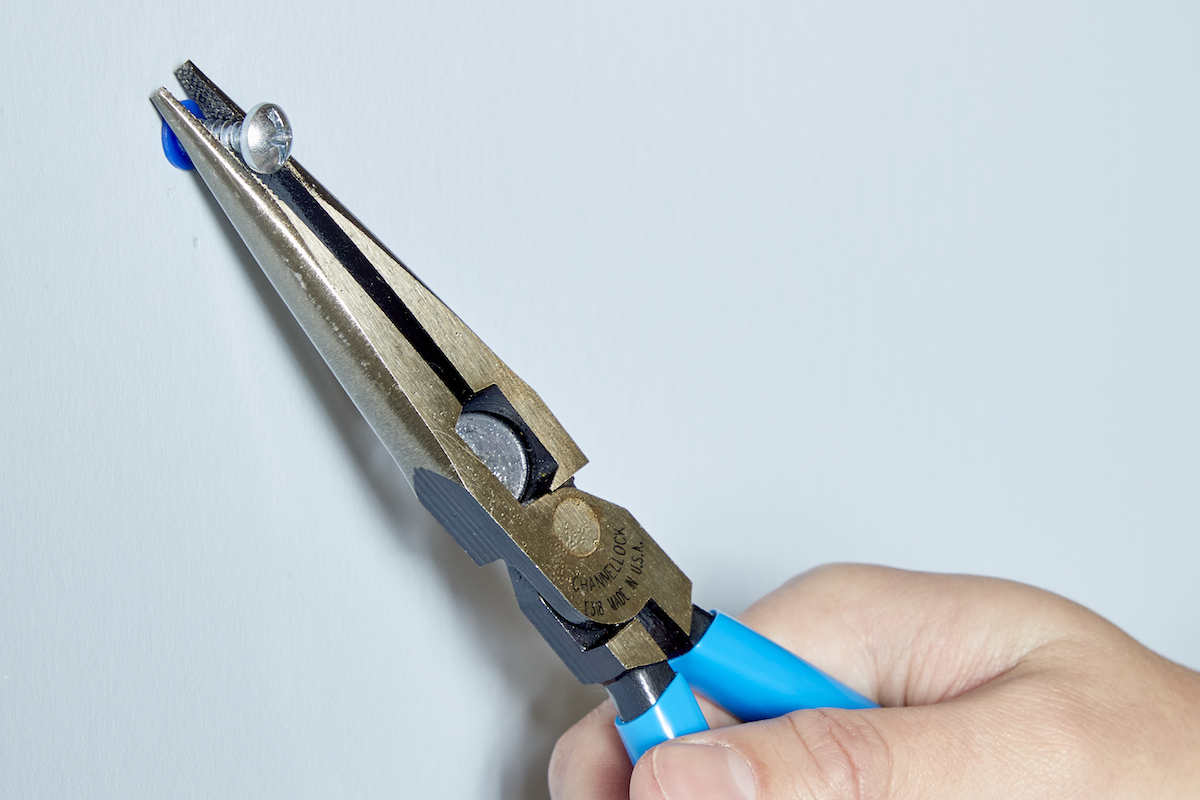 Woman uses needle-nose pliers to pull a screw out of a drywall anchor.