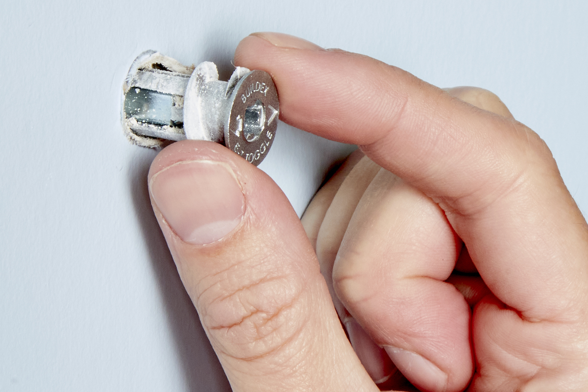 Woman pulls a self-drilling toggle anchor out of drywall.