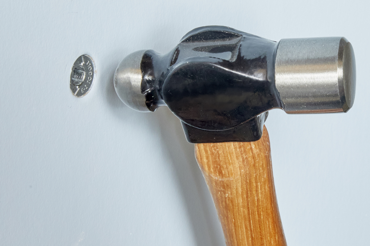 Using a ball peen hammer to recess a drywall anchor in the wall.