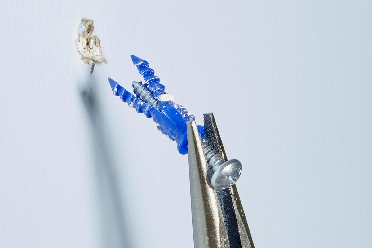 Woman uses needle-nose pliers to pull a screw and expansion anchor out of the wall.