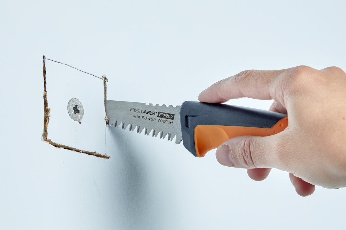 Woman uses a small saw to cut a drywall anchor out of a wall. 