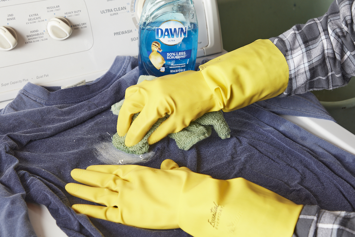 Woman wearing rubber gloves uses dish soap and a rag to remove a paint stain from a blue shirt.