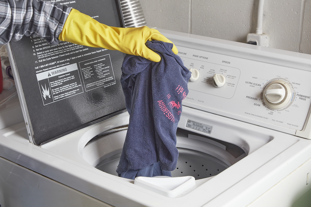 Woman wearing yellow rubber gloves places a blue T-shirt inside a top-load washing machine.