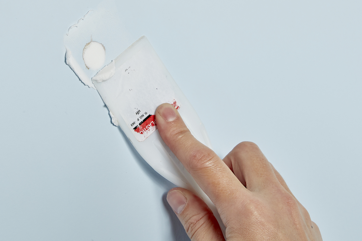 Woman uses a plastic putty knife to scrape excess spackle off a wall.