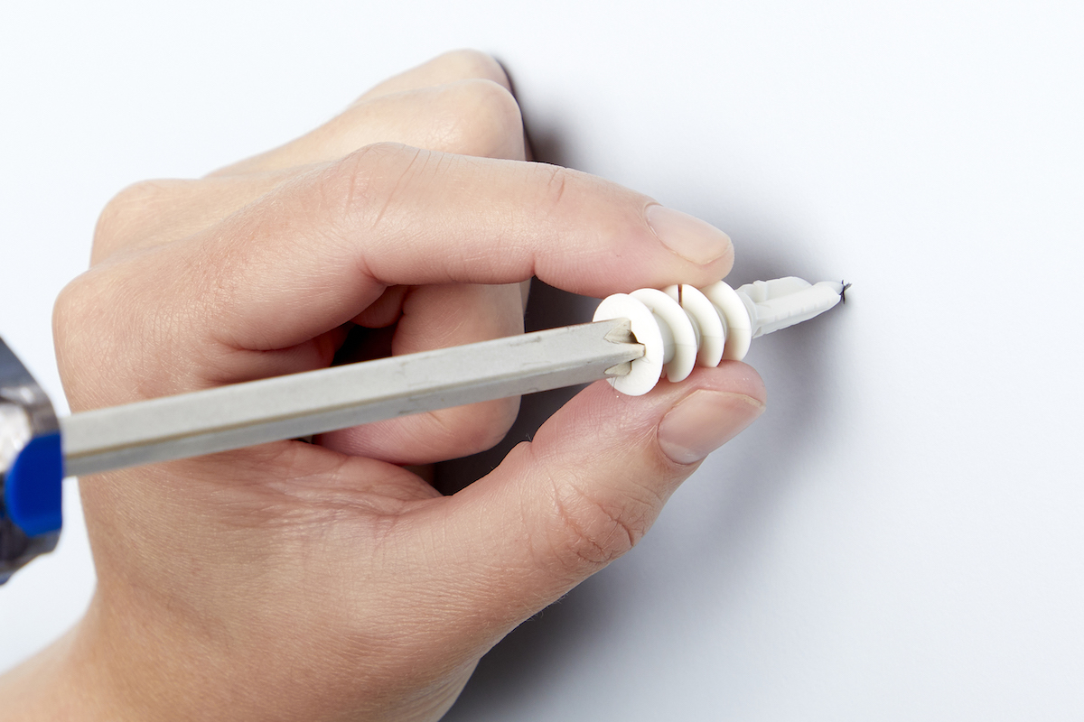 Woman puts the tip of a drywall anchor into a wall using a screwdriver.