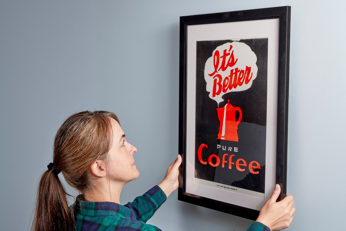 Woman hangs a poster that says "it's better pure coffee" on the wall.