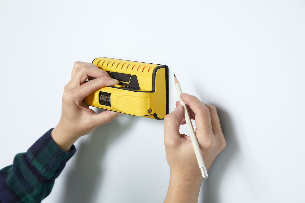 Woman uses a stud finder and marks their location with a pencil. 