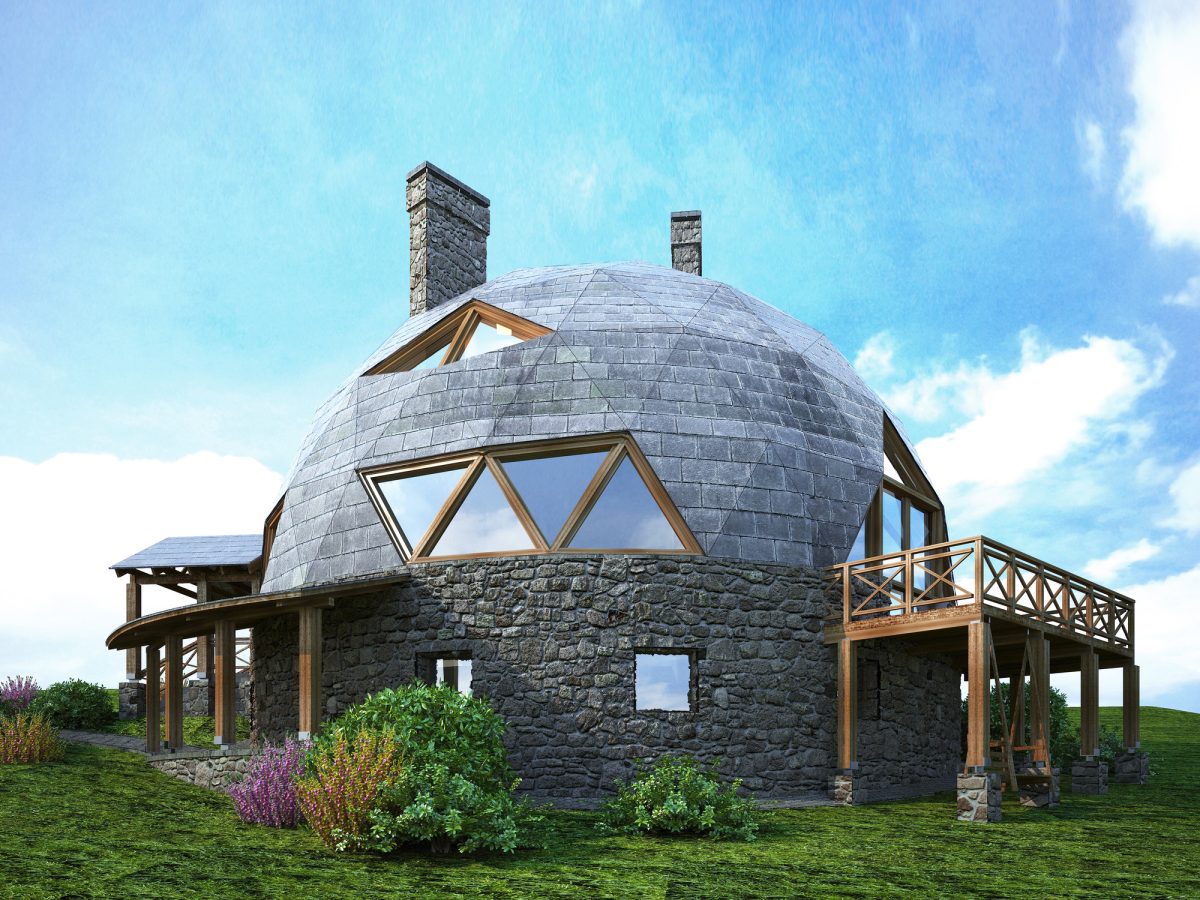A dome house with triangular windows and a wraparound wood deck stands on a green hill.