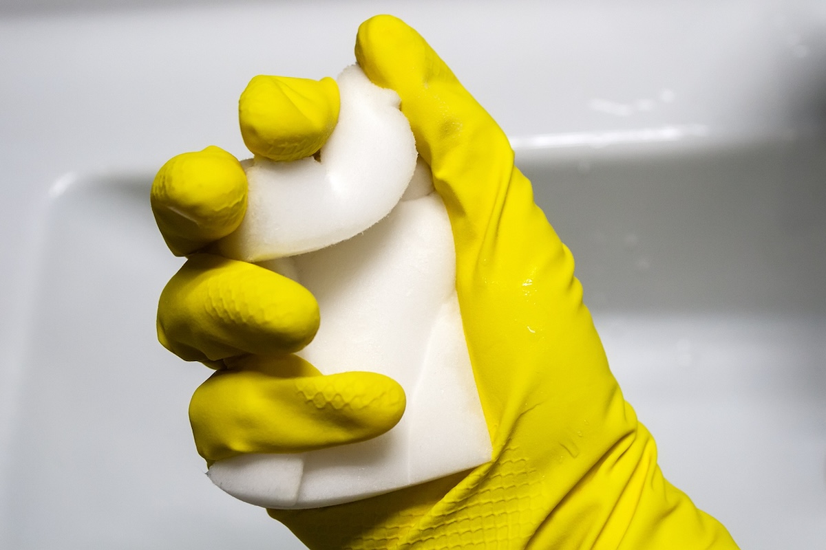 A person with a cleaning glove squeezing a magic eraser melamine sponge.