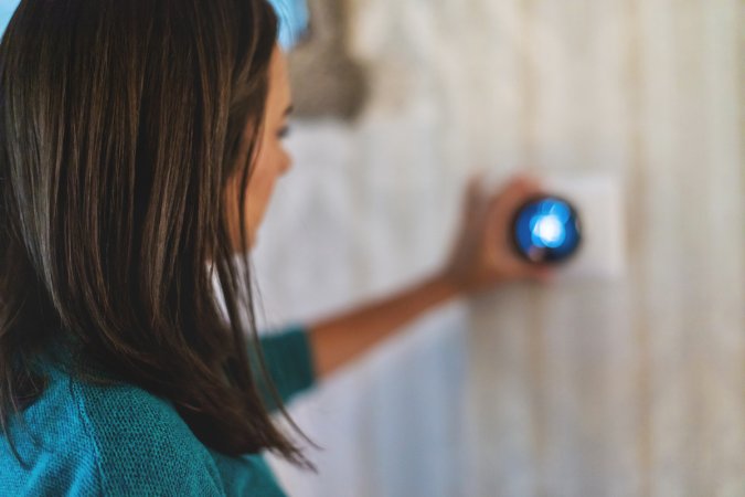 A woman is using a digital thermostat to change the air conditioning temperature.