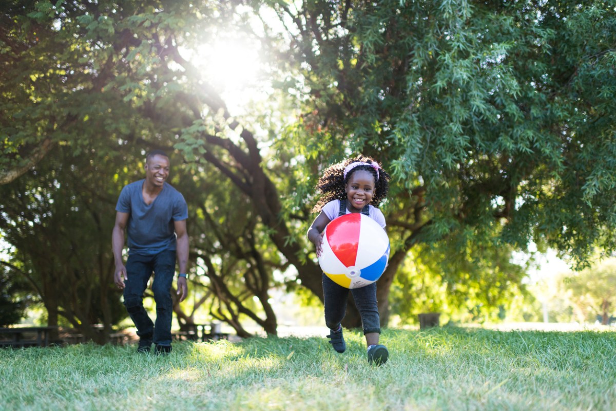 Happy little girl playing with a beach ball in the grass with her father