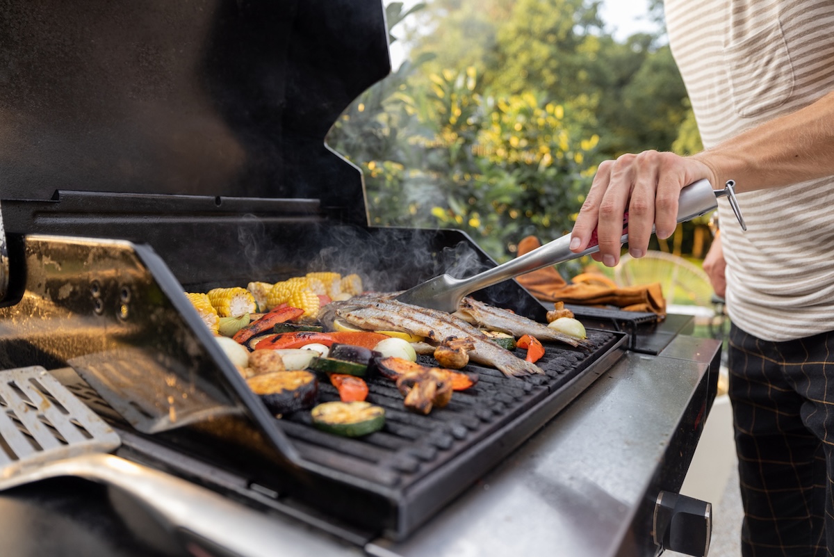 A person grilling on a natural gas grill in a suburban backyard.