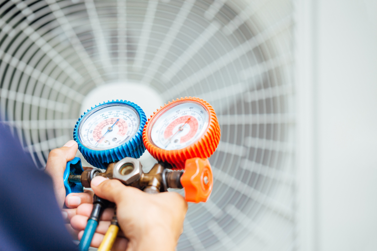 An air conditioning technician is using a gauge tool to test an outdoor air conditioning machine.