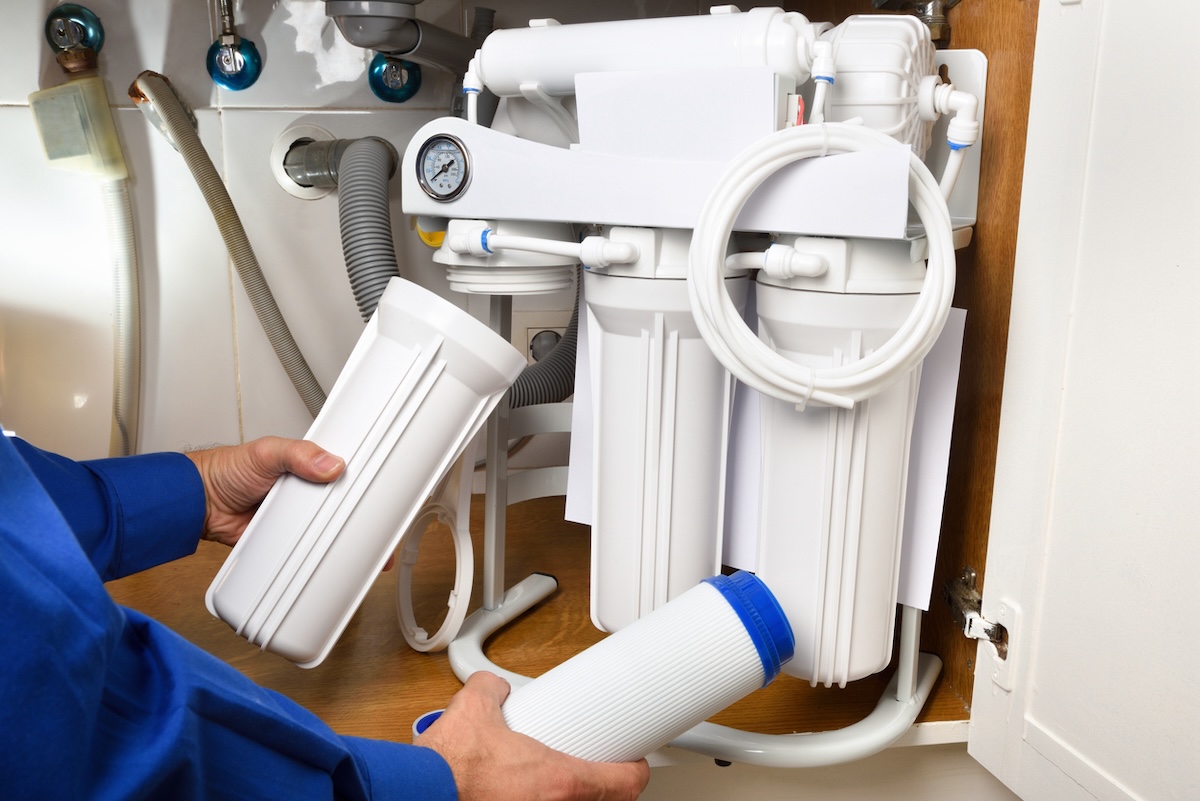 A person installing a reverse osmosis water filtration system in a residential home.