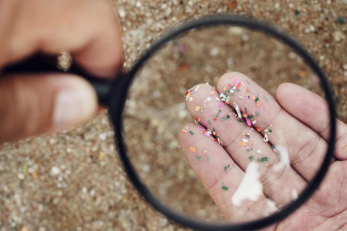 A person holding microplastics in their hand and viewing them through a magnifying glass.