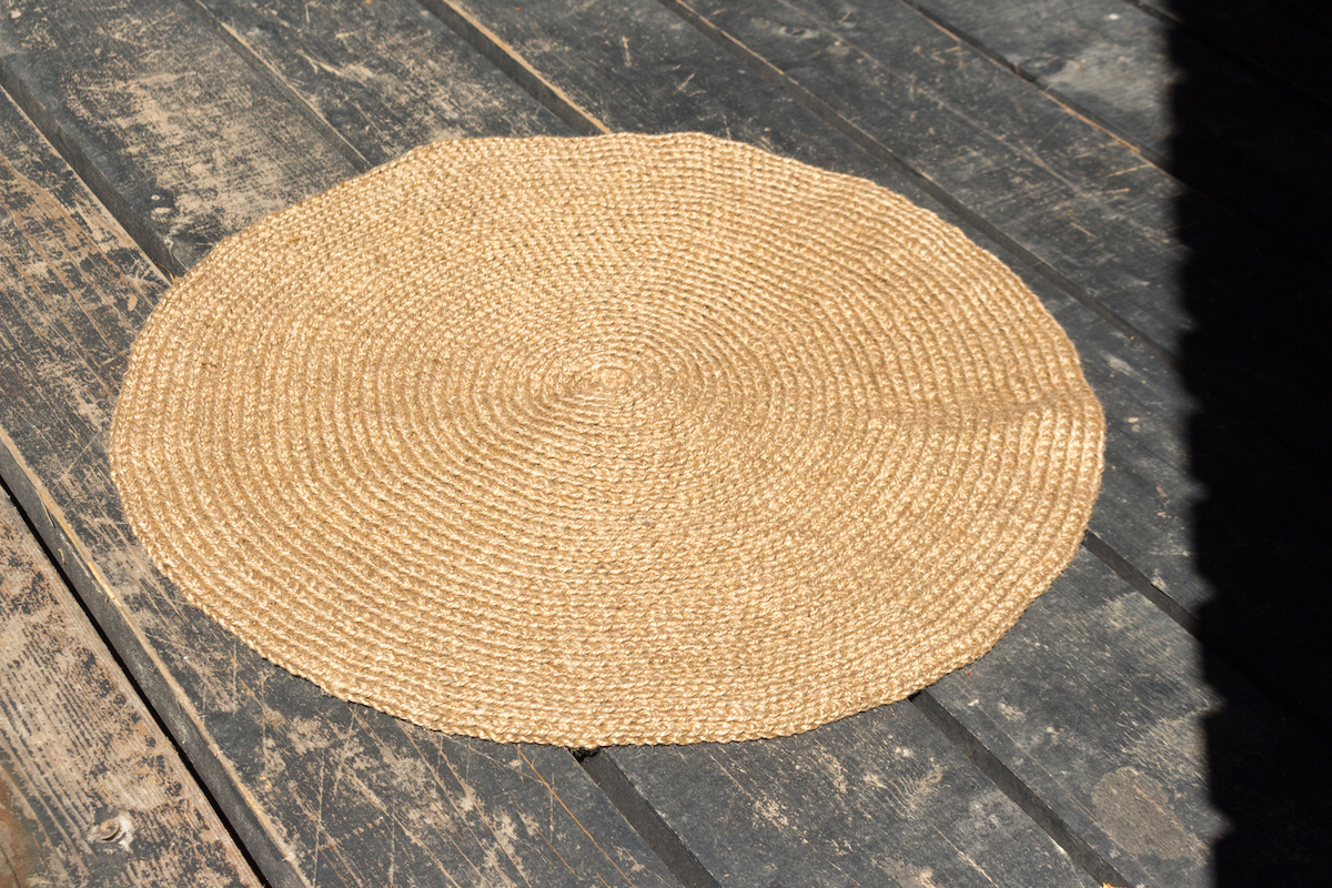 A handmade jute rope rug lies on a black wooden floor.