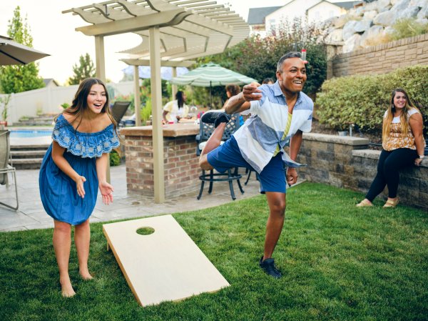 A group of friends playing a Cornhole bean bag toss game in a backyard of a home.