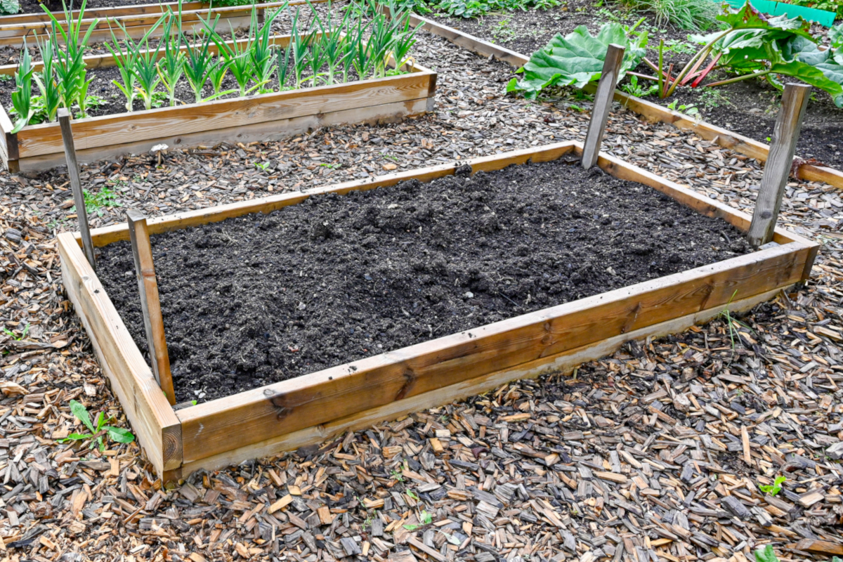 A newly built raised garden bed looks ready for planting after being filled with rich soil.