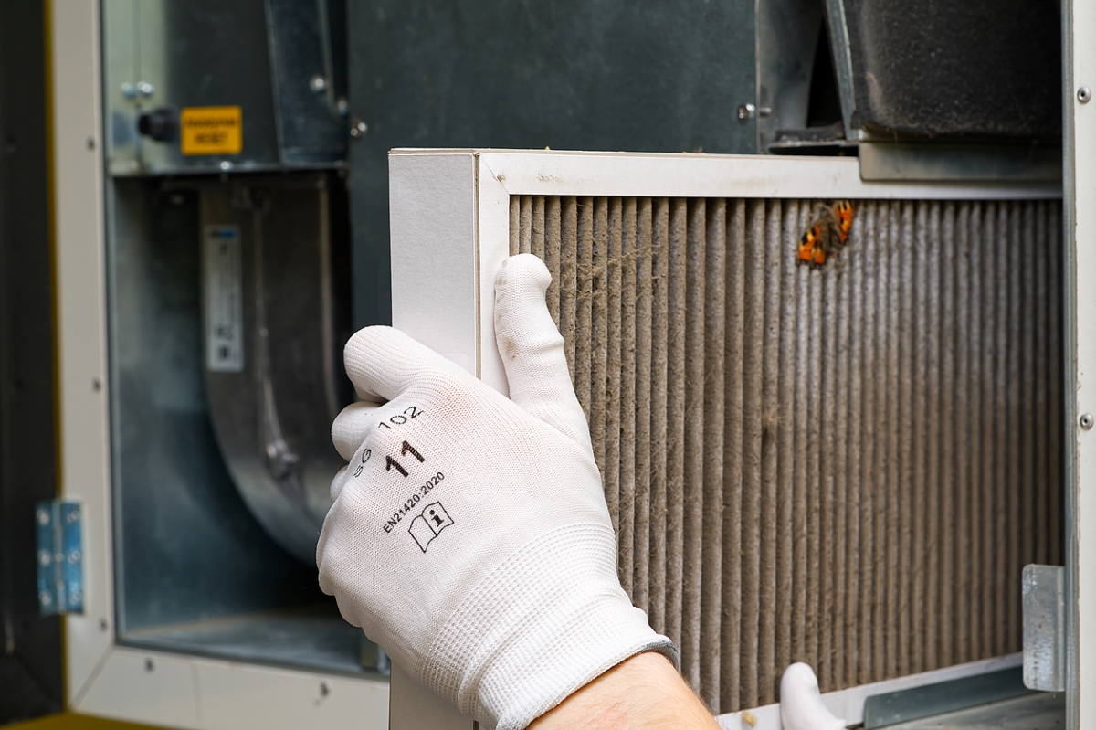 A gloved hand is removing a dirty filter from heat pump unit.