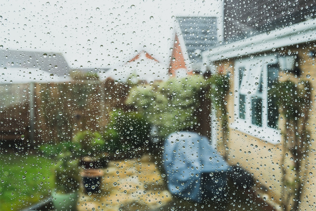 A window with rain droplets looking onto a backyard patio during a rain storm.