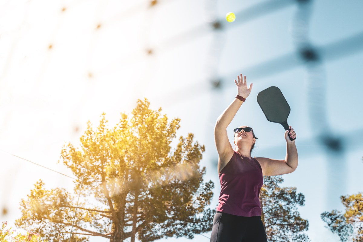 A person serves a pickleball in the sunshine.