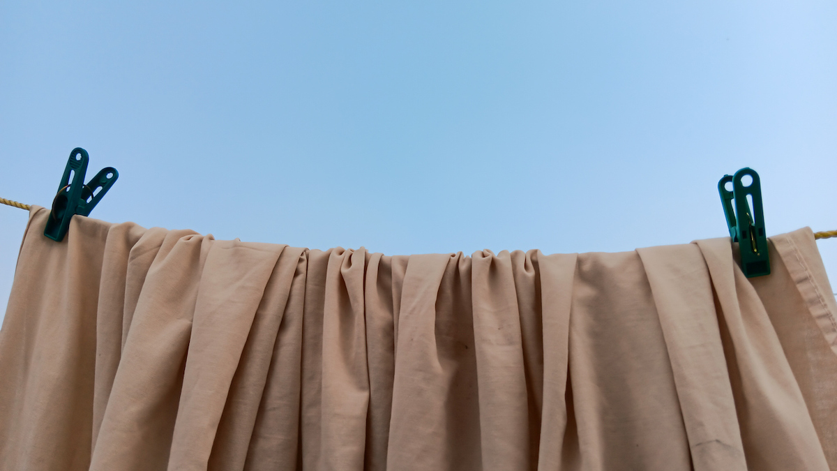 A beige curtain is hanging onto a clothesline outside with two clips.