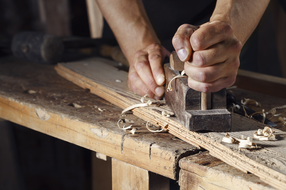 A carpenter is using a hand planer on a plank of wood.
