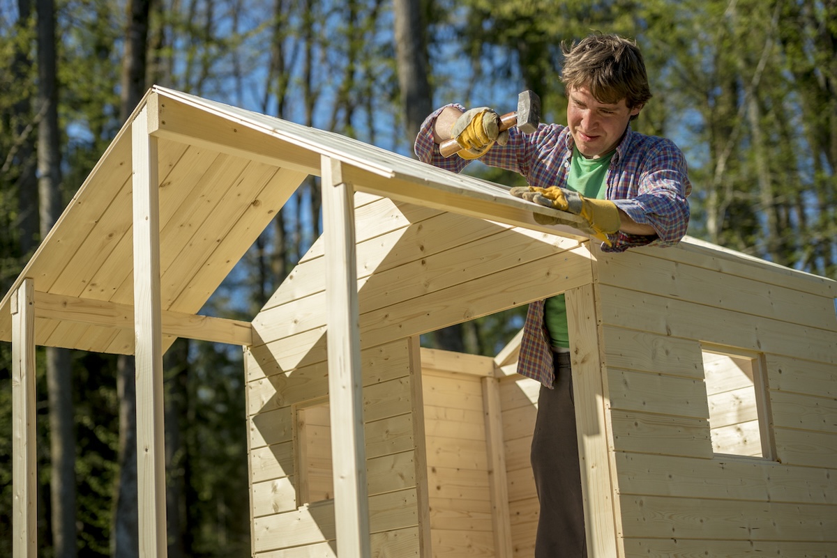 A person nailing roof sheathing on a kids playhouse.