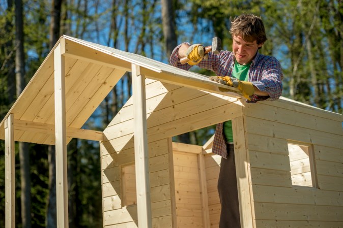 A person nailing roof sheathing on a kids playhouse.
