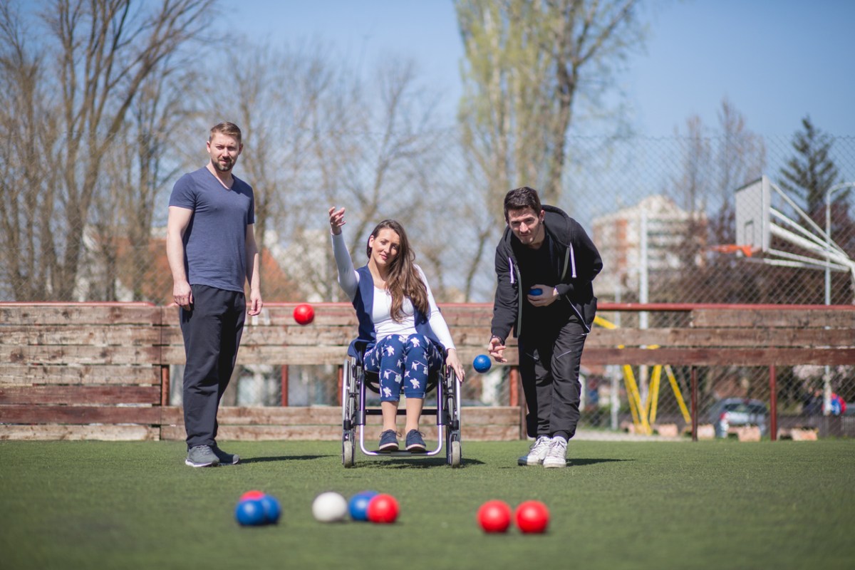 A young woman in a wheelchair and friends are playing bocce ball.