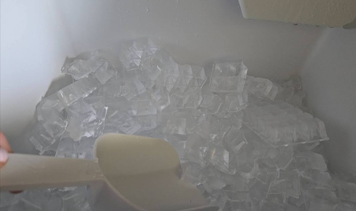 A person is collecting ice in a commercial ice maker with a plastic hand scoop.